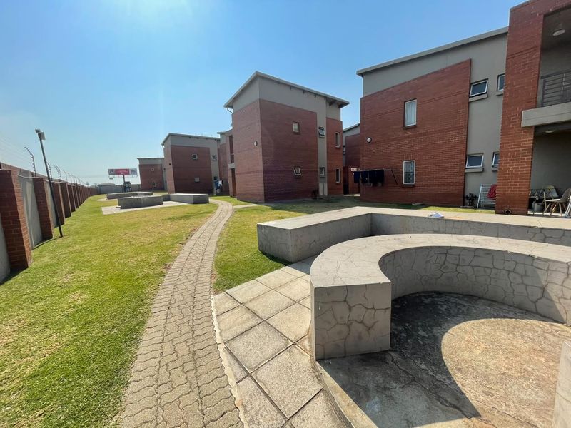 Communal outdoor area featuring brick apartment buildings, paved walkways, and concrete seating structures within a secure complex.