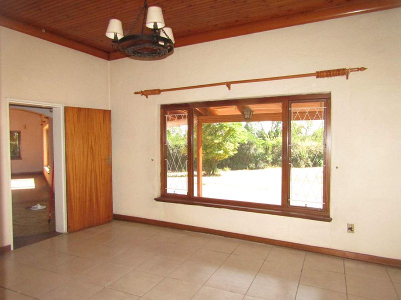 An empty living room featuring a timber ceiling, tiled flooring, and a large window with security bars overlooking the garden.