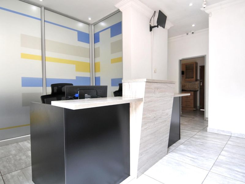 A professional reception area featuring a modern built-in desk, glass partition wall, and clean tiled flooring with recessed lighting.
