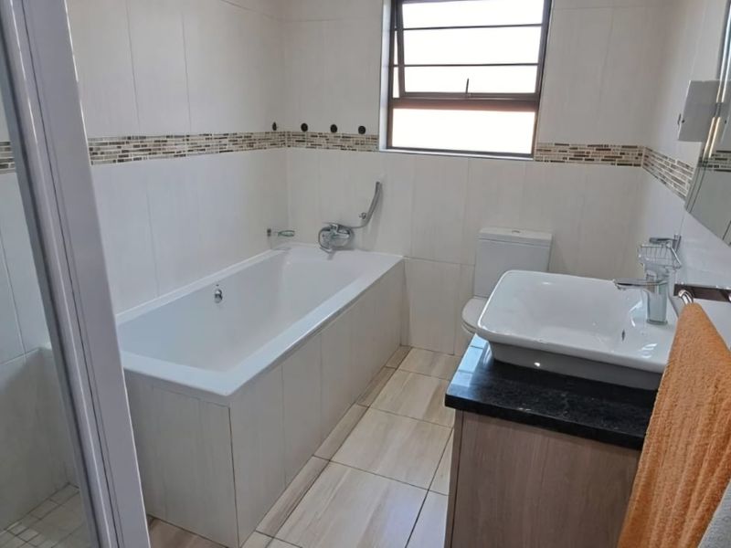 A clean, modern bathroom featuring a built-in bathtub, separate shower enclosure, vanity with granite countertop, and neutral wall tiling with decorative accents.