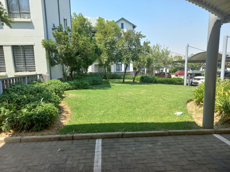 A well-maintained communal garden area featuring a manicured lawn, established shrubbery, and adjacent paved parking spaces within the apartment complex.