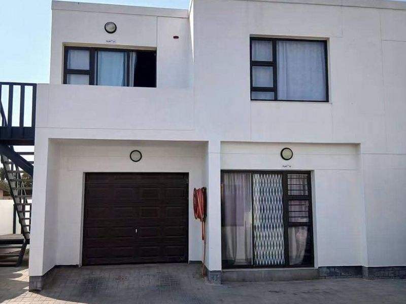 Front elevation of a modern townhouse featuring a paved driveway, single garage, and external staircase leading to the upper level.