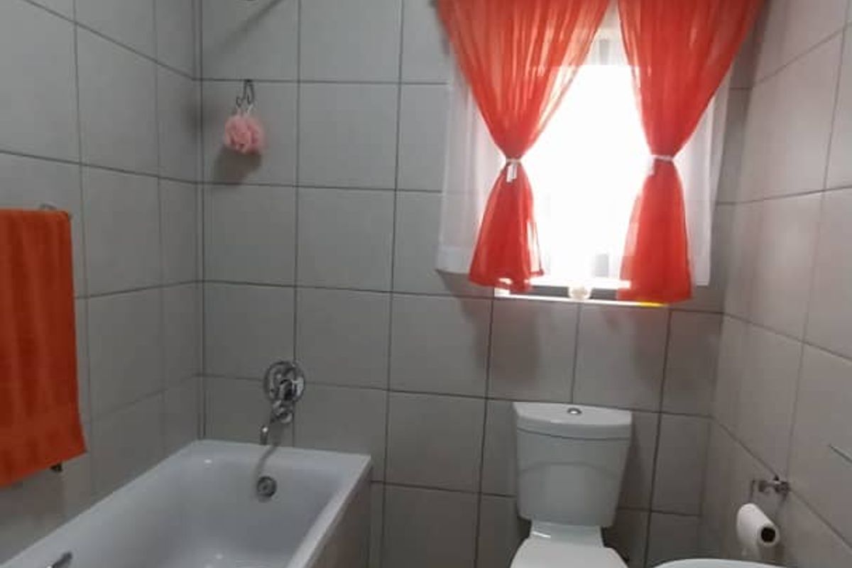 A functional bathroom featuring a bathtub with shower head, pedestal basin, and toilet, finished with neutral wall and floor tiling.