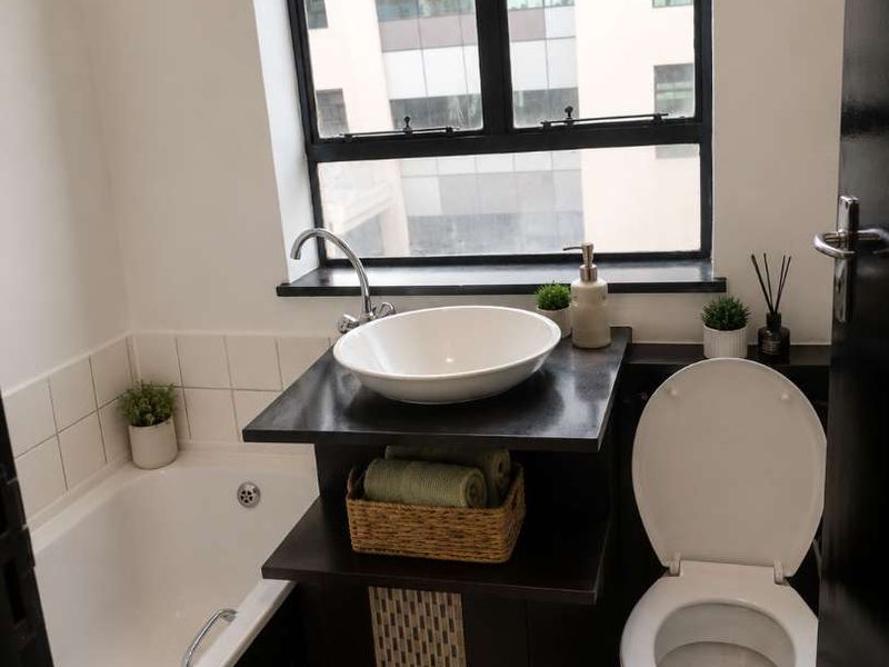 Compact bathroom featuring a bathtub, vessel sink vanity, and toilet, complemented by a large window providing natural light.