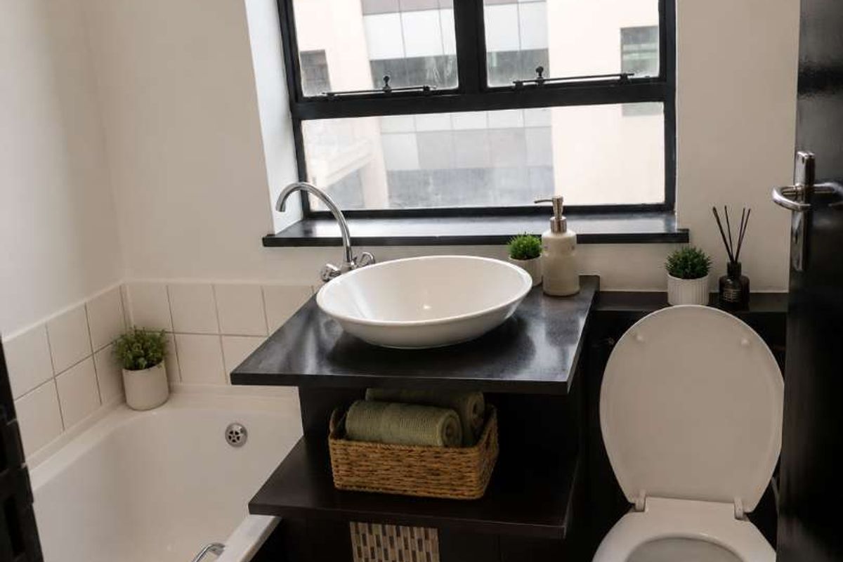 Compact bathroom featuring a bathtub, vessel sink vanity, and toilet, complemented by a large window providing natural light.
