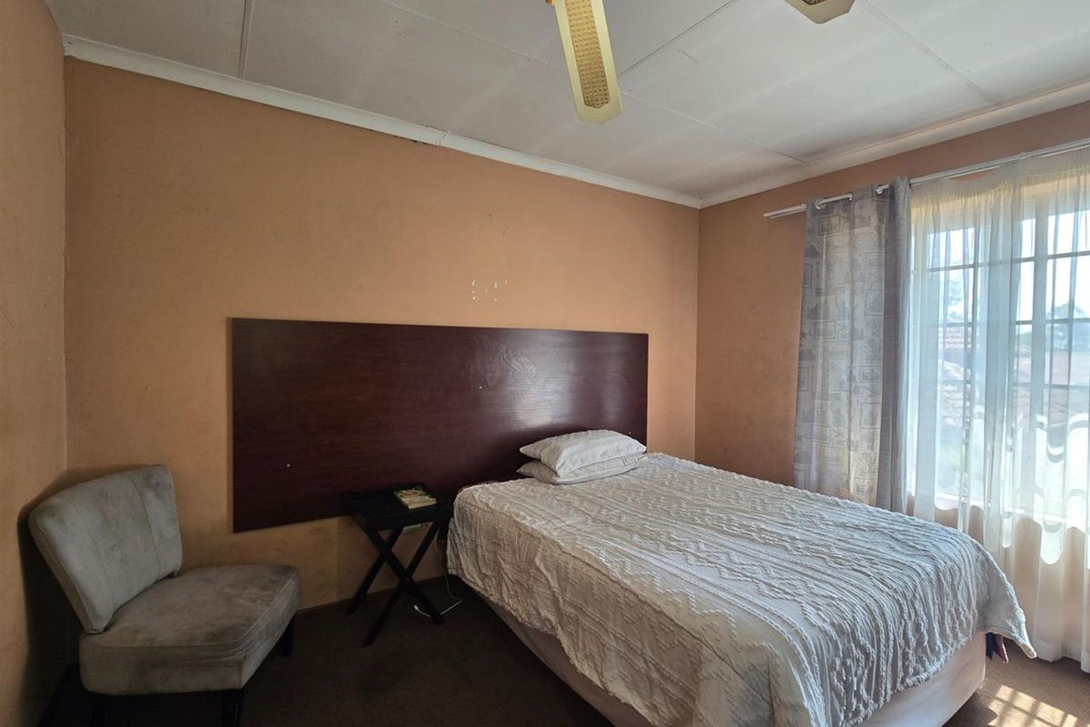 A bedroom featuring a built-in dark wood headboard, ceiling fan, and carpeted flooring, offering a functional space with potential for cosmetic updates.