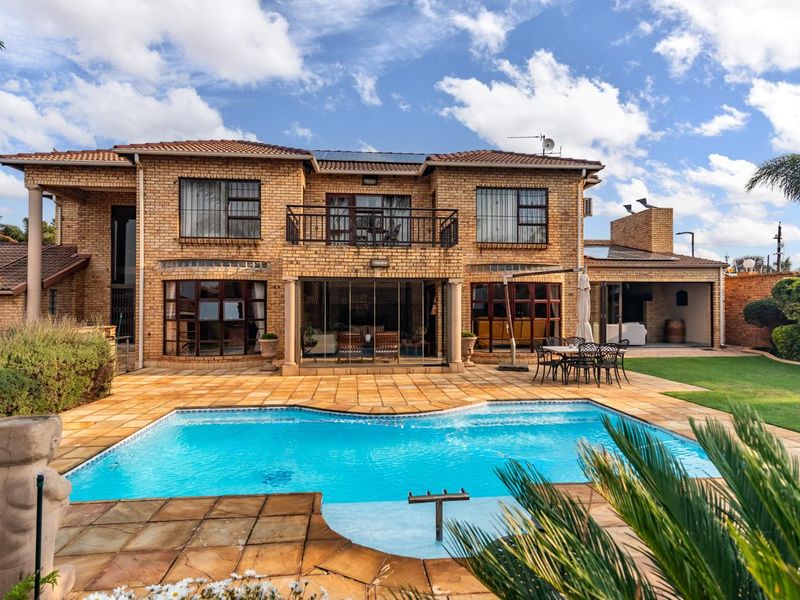 Rear view of a double-story brick house featuring a swimming pool, paved patio area, and an upper-level balcony.