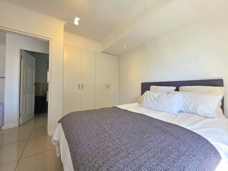 A well-maintained bedroom featuring neutral tiled flooring, built-in cupboards, and recessed lighting, with an adjoining doorway leading to an ensuite bathroom.
