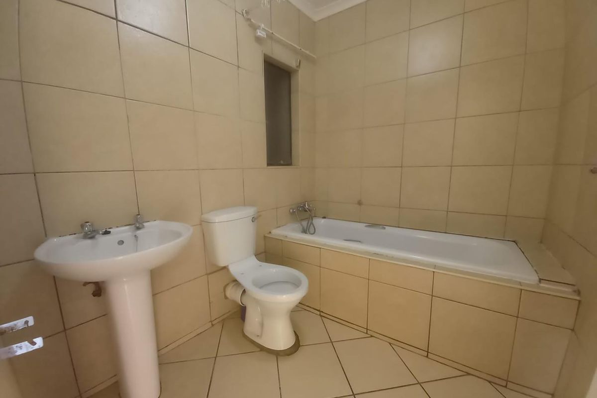 A functional bathroom featuring a pedestal basin, toilet, and a built-in bathtub with full-height wall tiling.