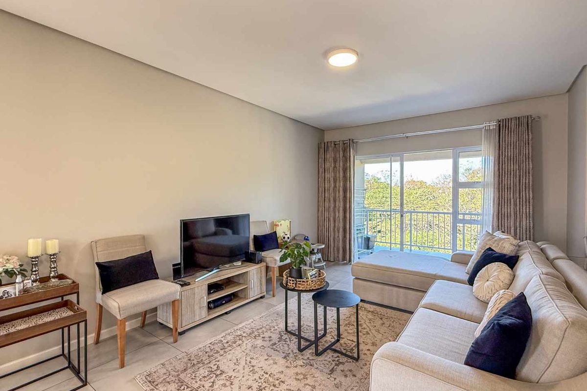 A bright and comfortable living room featuring large sliding glass doors that open onto a private balcony with scenic green views.