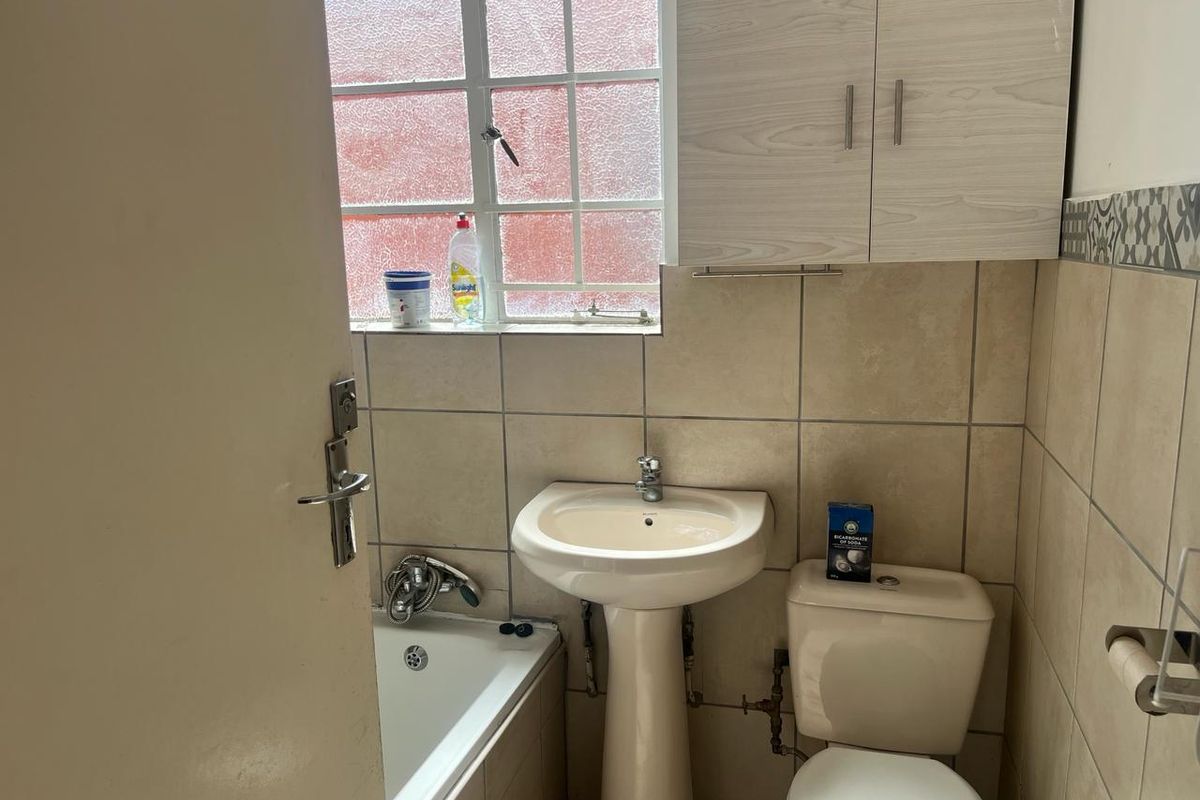 A functional bathroom featuring a pedestal basin, standard toilet, and a bathtub with tiled walls and a window for natural light.