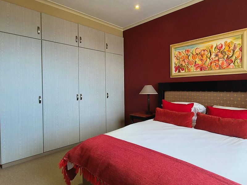 A well-maintained bedroom featuring extensive built-in cupboards, neutral carpeting, and a bold accent wall.