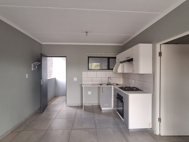 Open plan kitchen area featuring modern cabinetry, gas hob, built-in oven, and tiled flooring, leading to an outdoor balcony space.