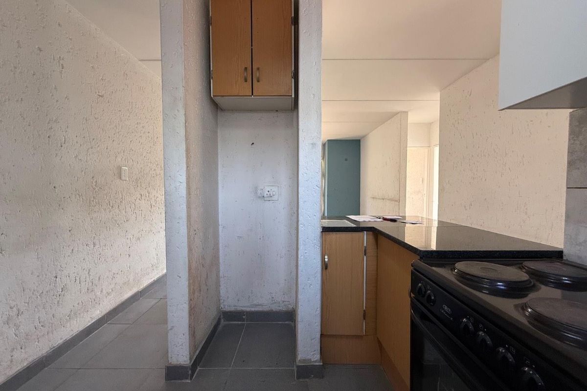 A dated kitchen area featuring built-in cabinetry, a granite countertop, and an electric stove, with tiled flooring and textured wall finishes.