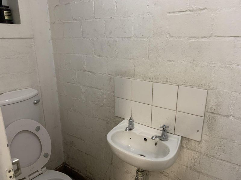A compact bathroom featuring a wall-mounted basin with a tiled splashback and a standard toilet, requiring cosmetic updates to the wall finishes.