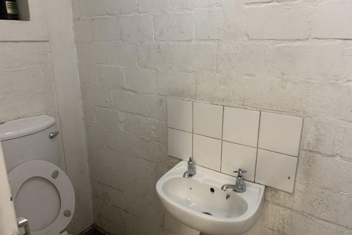 A compact bathroom featuring a wall-mounted basin with a tiled splashback and a standard toilet, requiring cosmetic updates to the wall finishes.