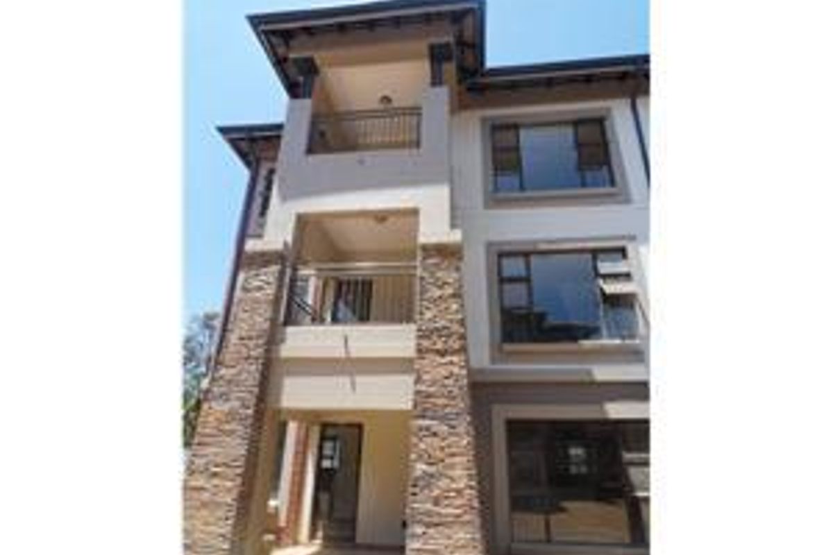 A modern multi-story apartment building facade featuring stone cladding, private balconies with stainless steel railings, and large aluminium-framed windows.