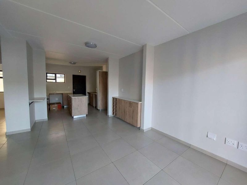 Spacious open-plan living and kitchen area featuring neutral tiled flooring, modern built-in cabinetry, and a functional kitchen island in a clean, well-maintained space.
