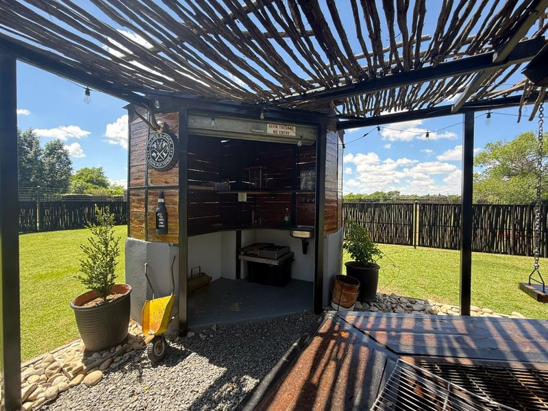 Outdoor entertainment area featuring a covered pergola, built-in braai station with sink, and gravel flooring, set within a landscaped garden.