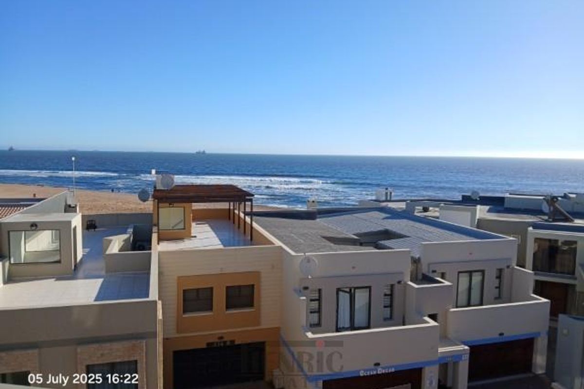 Elevated aerial view of a coastal apartment complex featuring modern architecture, flat roofs, and direct proximity to the ocean.