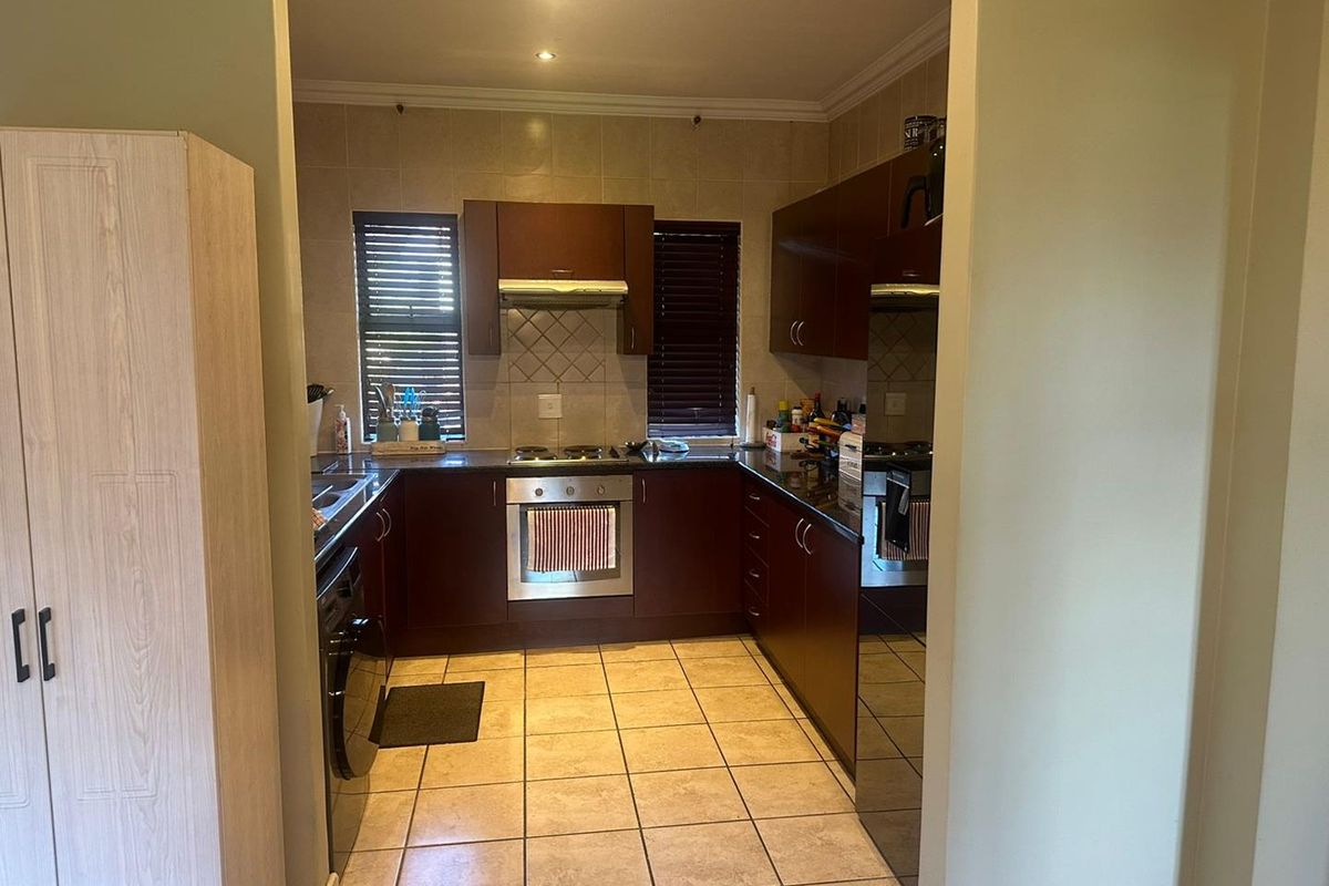 A functional U-shaped kitchen featuring dark wood cabinetry, tiled flooring, built-in oven, hob, and extractor fan, with integrated space for laundry appliances.