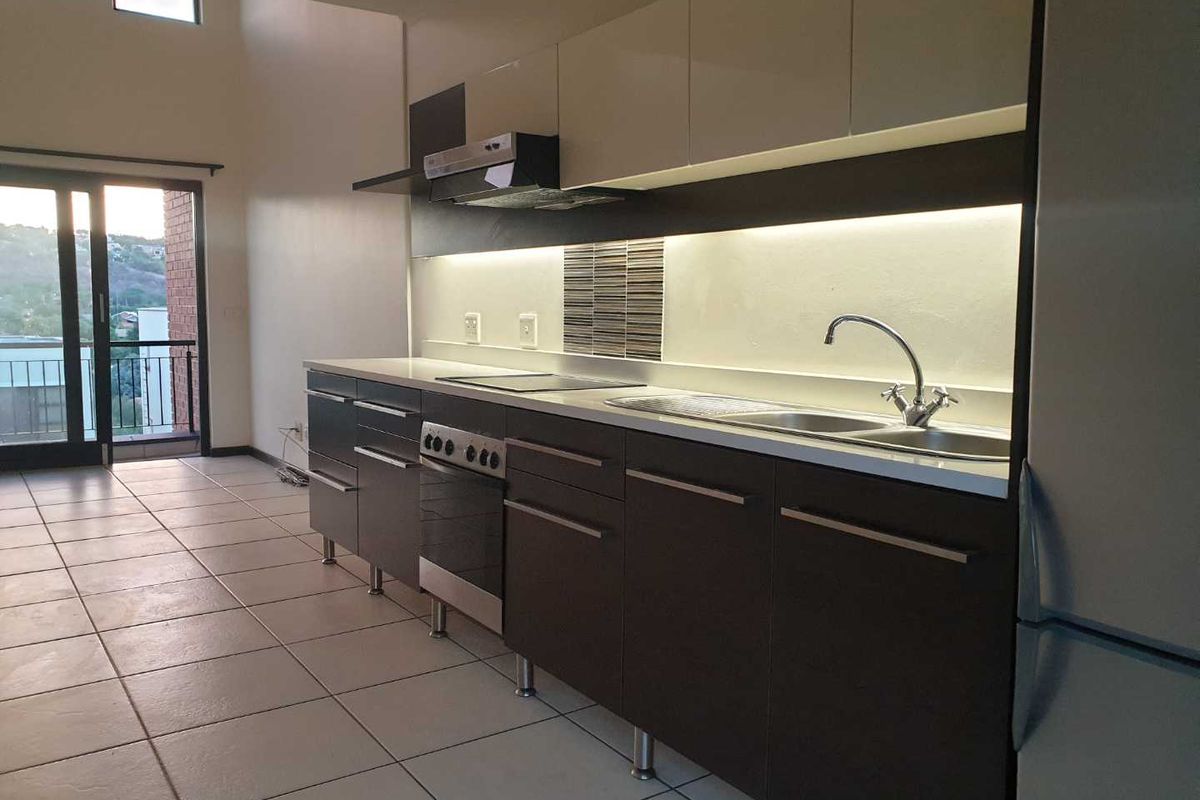 Modern kitchen featuring sleek dark lower cabinetry, light upper cabinets, integrated appliances, tiled flooring, and under-cabinet lighting, opening onto a balcony area.
