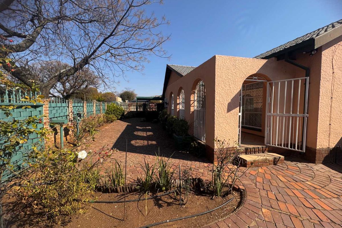 Rear exterior view featuring a brick-paved patio area, arched covered walkway, and secure perimeter fencing in a residential garden setting.