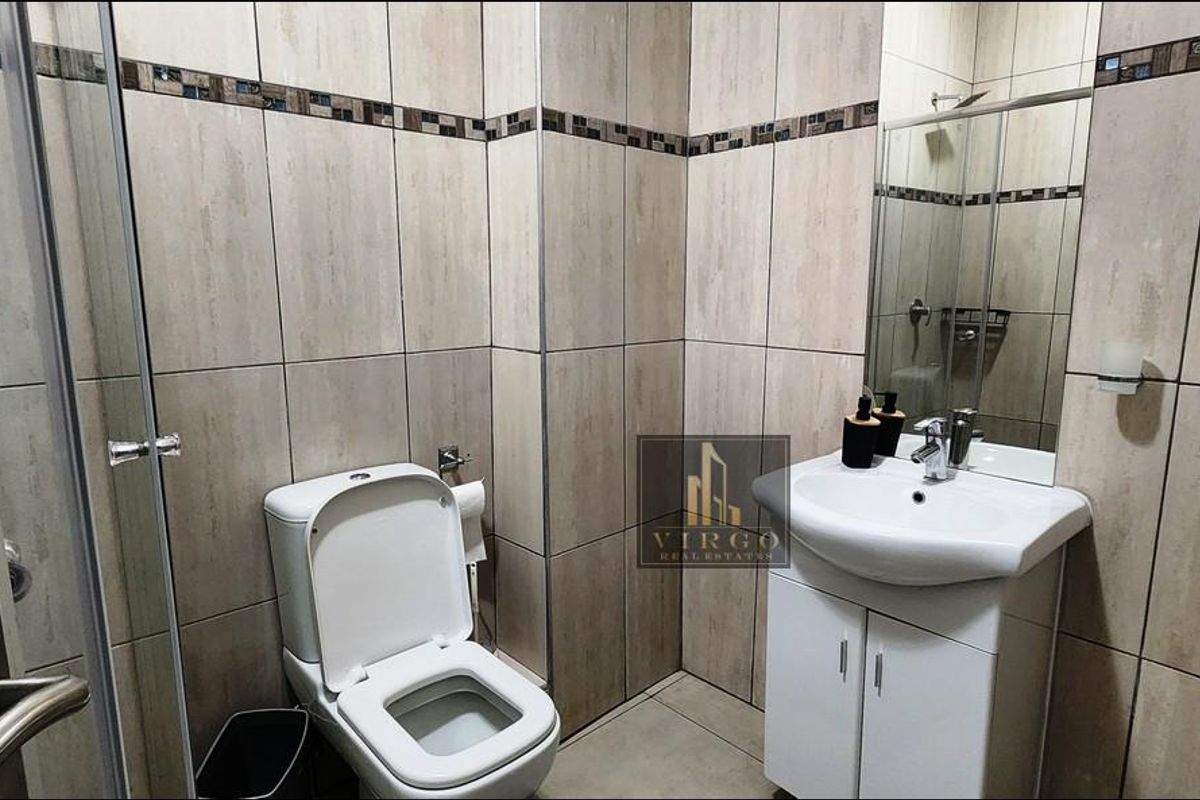 A clean, modern bathroom featuring tiled walls, a vanity cabinet with a washbasin, and a glass-enclosed shower.