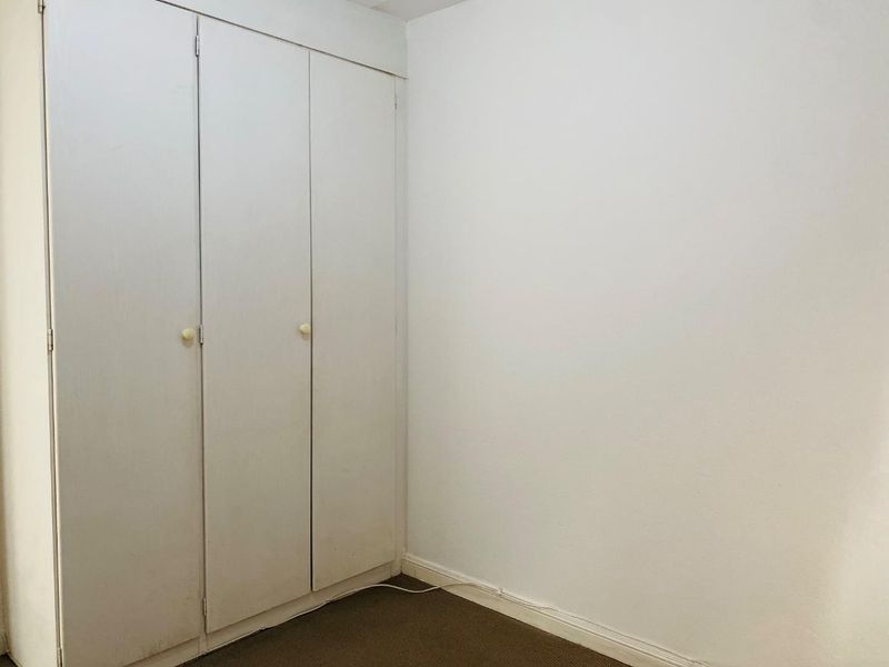 A simple, empty bedroom featuring a built-in wardrobe with white doors and neutral carpeting.