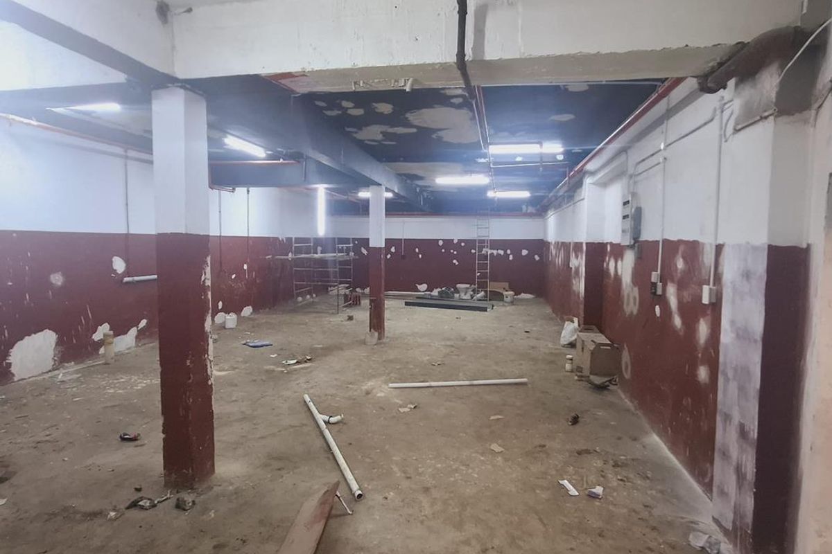 An expansive, open-plan industrial utility space featuring exposed ceilings, fire sprinkler infrastructure, and structural columns, currently in need of renovation and finishing.