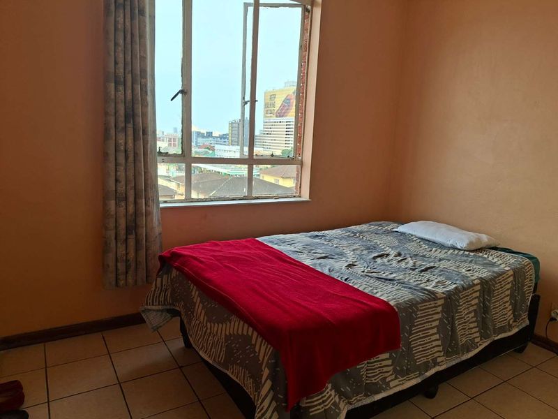 A bedroom featuring tiled flooring and a large window with urban views, requiring cosmetic updates to the wall finishes.