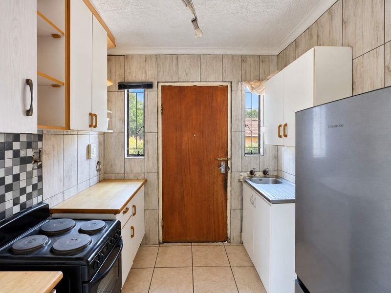 A compact kitchen featuring built-in cabinetry, a stainless steel sink, and tiled finishes, offering a functional layout with direct exterior access.
