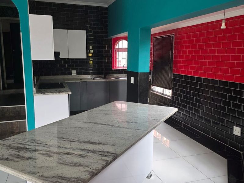 Modern kitchen featuring a granite-topped island, contrasting subway tile backsplash, and clean tiled flooring, offering a functional and contemporary culinary space.