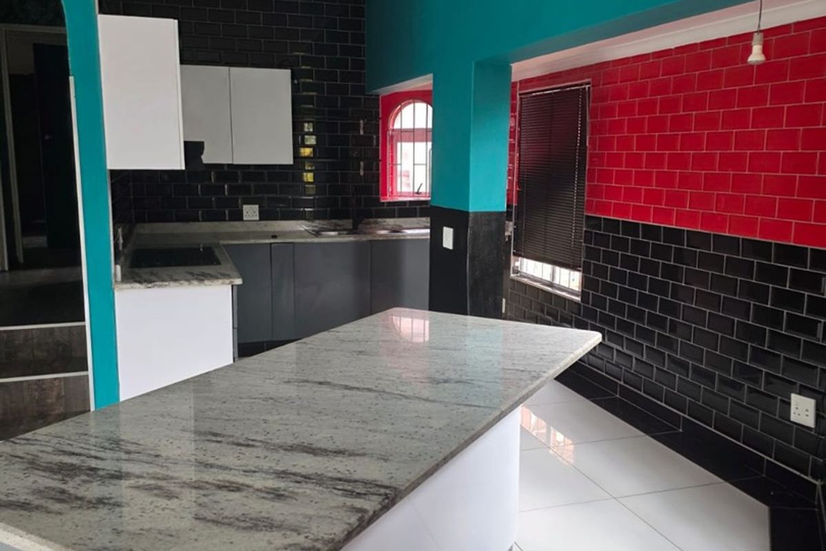 Modern kitchen featuring a granite-topped island, contrasting subway tile backsplash, and clean tiled flooring, offering a functional and contemporary culinary space.