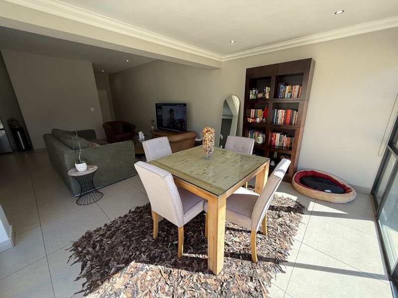 An open-plan living and dining area featuring neutral tiled flooring, recessed downlighting, and crown molding, creating a bright and functional living space.