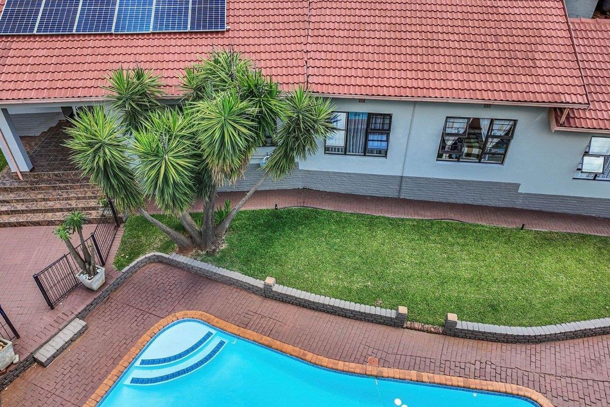 Aerial view of the rear exterior featuring a swimming pool, paved patio area, landscaped garden, and solar panels installed on the tiled roof.