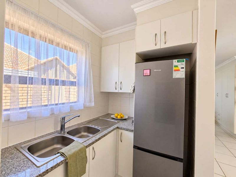 A compact, well-maintained kitchen featuring white cabinetry, granite countertops, and a double bowl stainless steel sink with a modern chrome mixer tap.