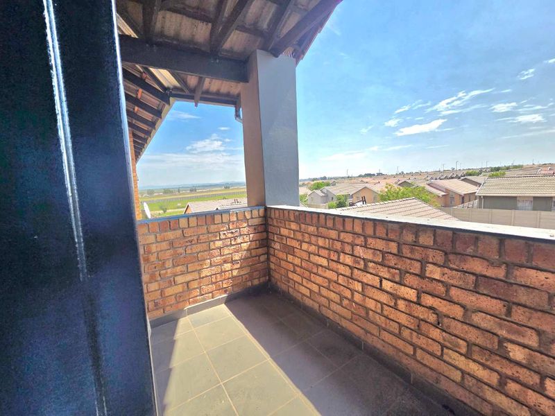 A covered balcony featuring exposed brick walls, tiled flooring, and an open view of the surrounding residential area.