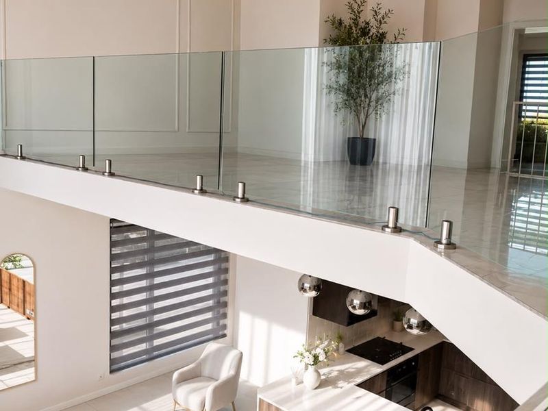 Modern open-plan living area featuring a sleek kitchen with island, glass balustrade mezzanine, and high-end finishes throughout.