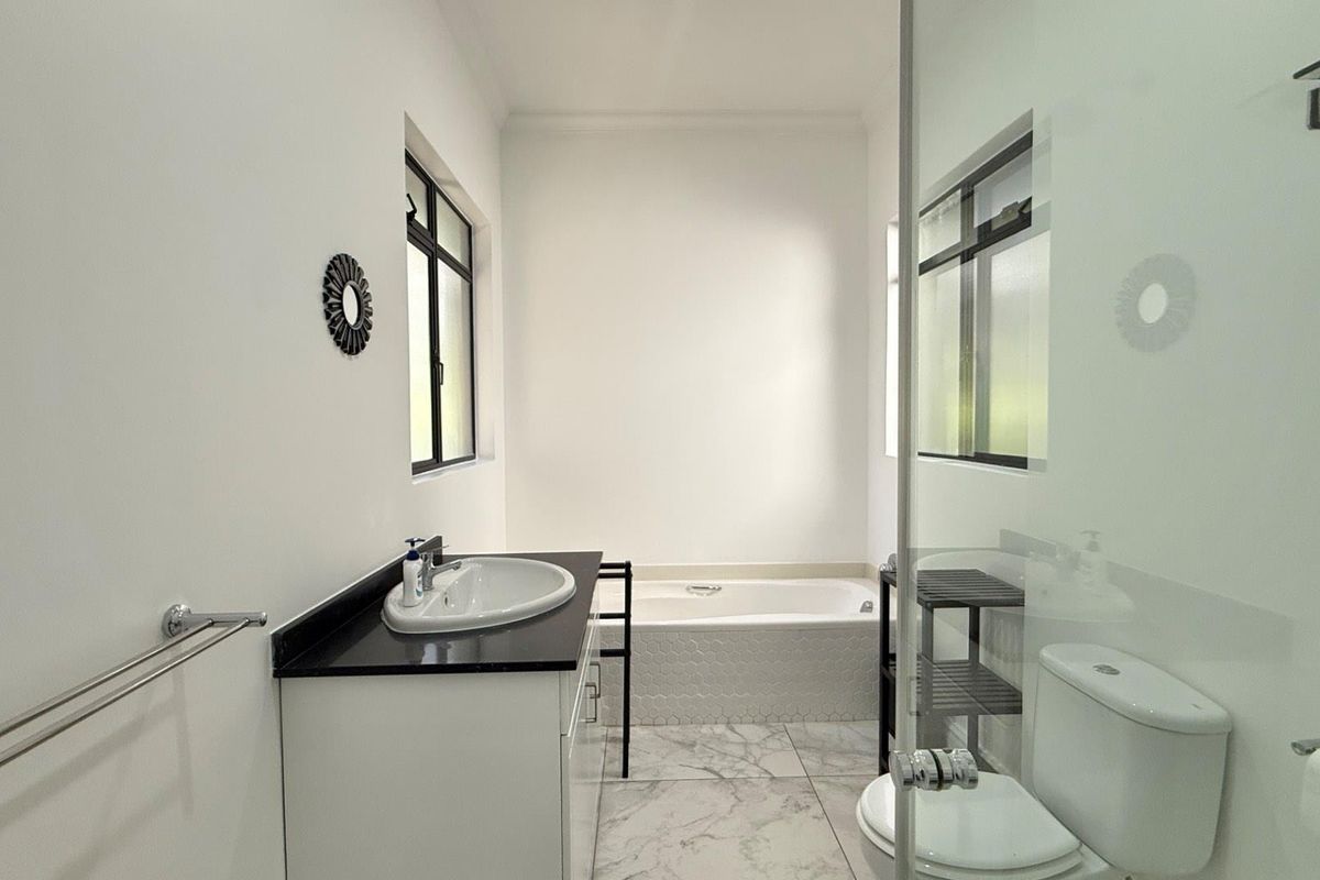 A modern bathroom featuring a vanity with a dark countertop, a built-in bathtub, a glass-enclosed shower, and marble-style floor tiles.