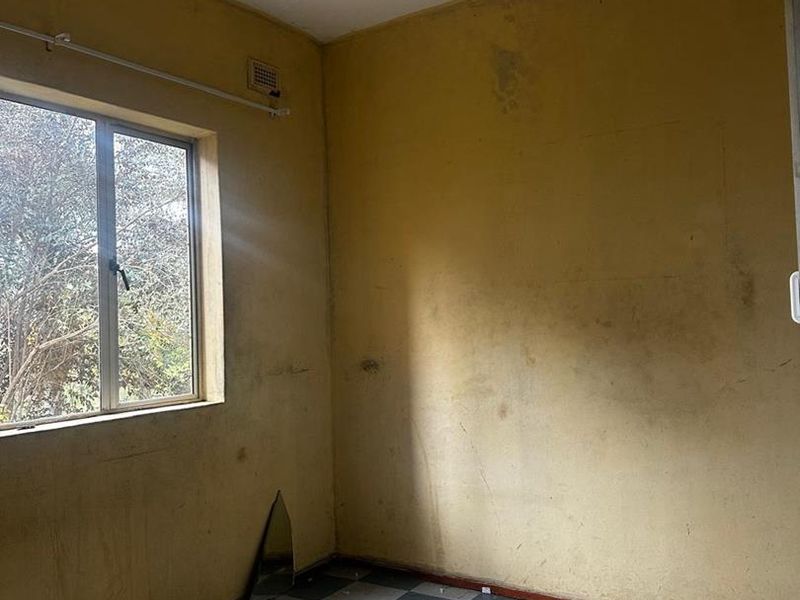 An empty bedroom featuring checkered floor tiles and yellow walls in need of cosmetic refurbishment and painting.