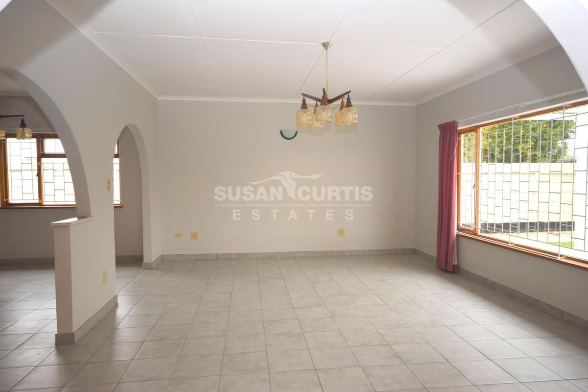 A spacious, empty living room featuring neutral tiled flooring, an arched entryway, and large windows fitted with security bars.