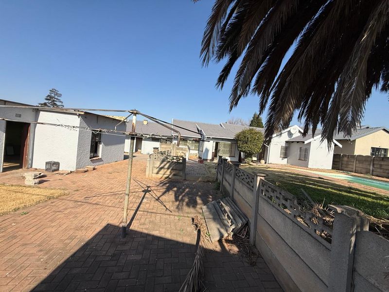 Rear exterior view of the property featuring a paved patio area, precast boundary wall, and a swimming pool in the garden.