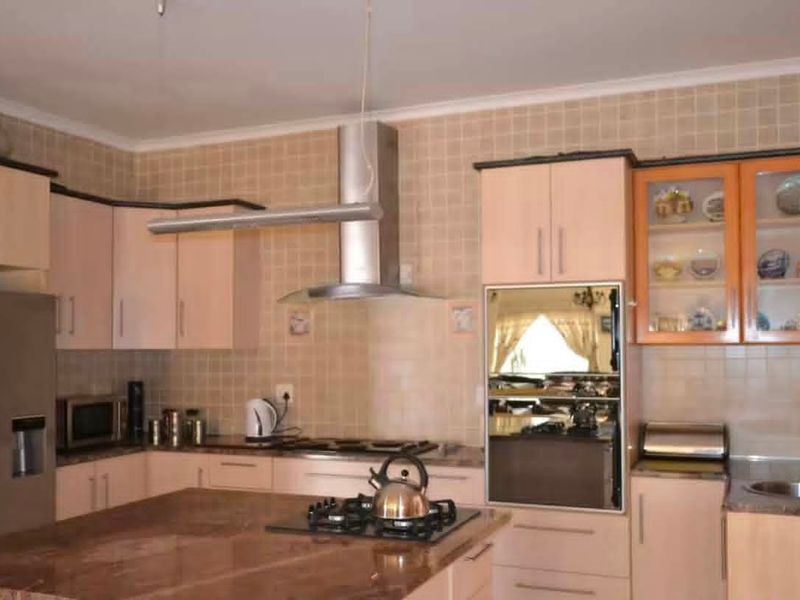 A functional kitchen featuring granite countertops, built-in cabinetry, a gas hob, and a stainless steel extractor fan with a tiled backsplash.