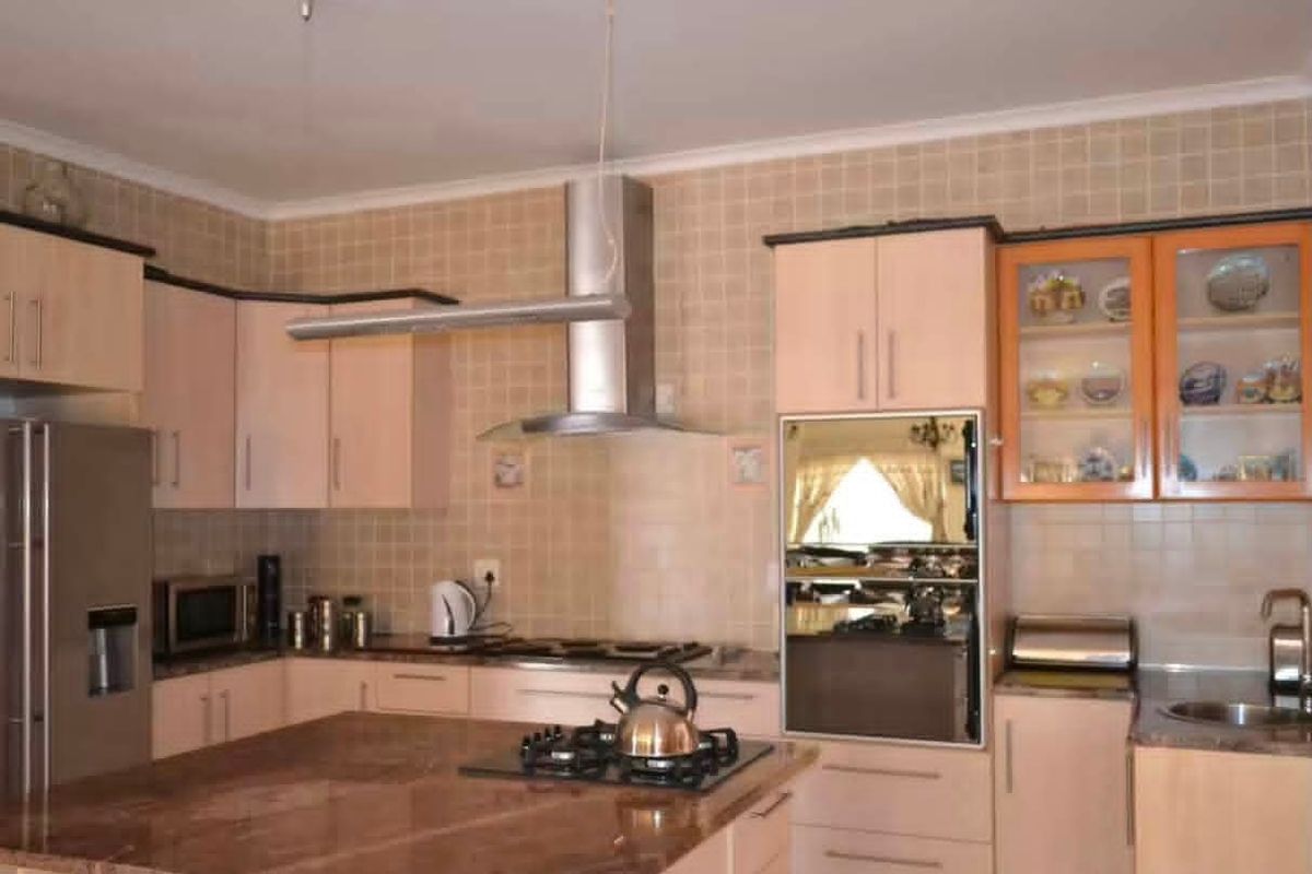 A functional kitchen featuring granite countertops, built-in cabinetry, a gas hob, and a stainless steel extractor fan with a tiled backsplash.
