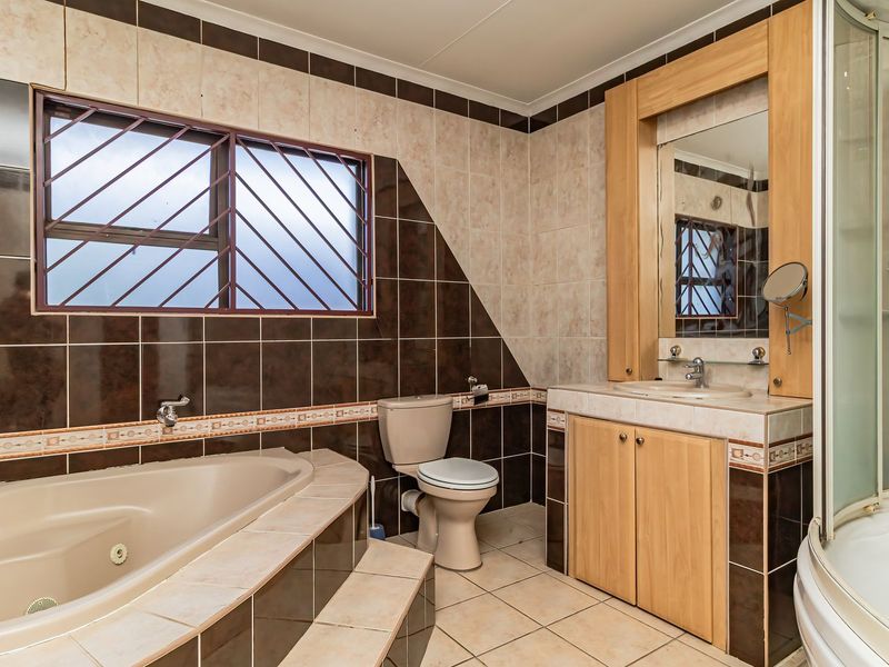 A spacious bathroom featuring a built-in bathtub, separate shower enclosure, and a wooden vanity cabinet with an integrated mirror.