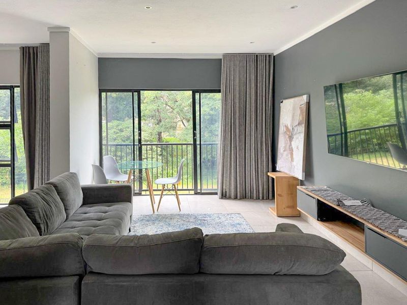 A modern living room featuring tiled floors, recessed lighting, and large sliding glass doors that open to a balcony with green views.