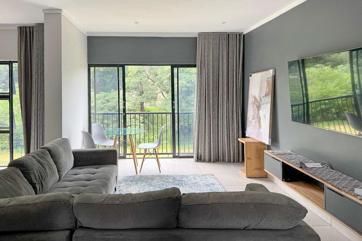 A modern living room featuring tiled floors, recessed lighting, and large sliding glass doors that open to a balcony with green views.
