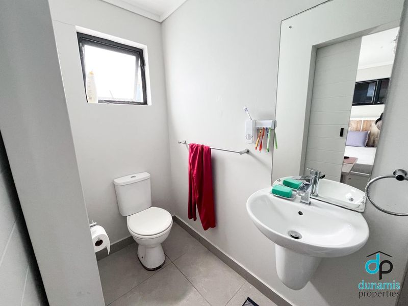 A clean and functional bathroom featuring a pedestal basin, toilet, tiled flooring, and a wall-mounted mirror.