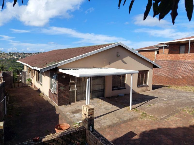 Rear view of the property featuring a covered patio area, paved yard, and brick boundary walling.